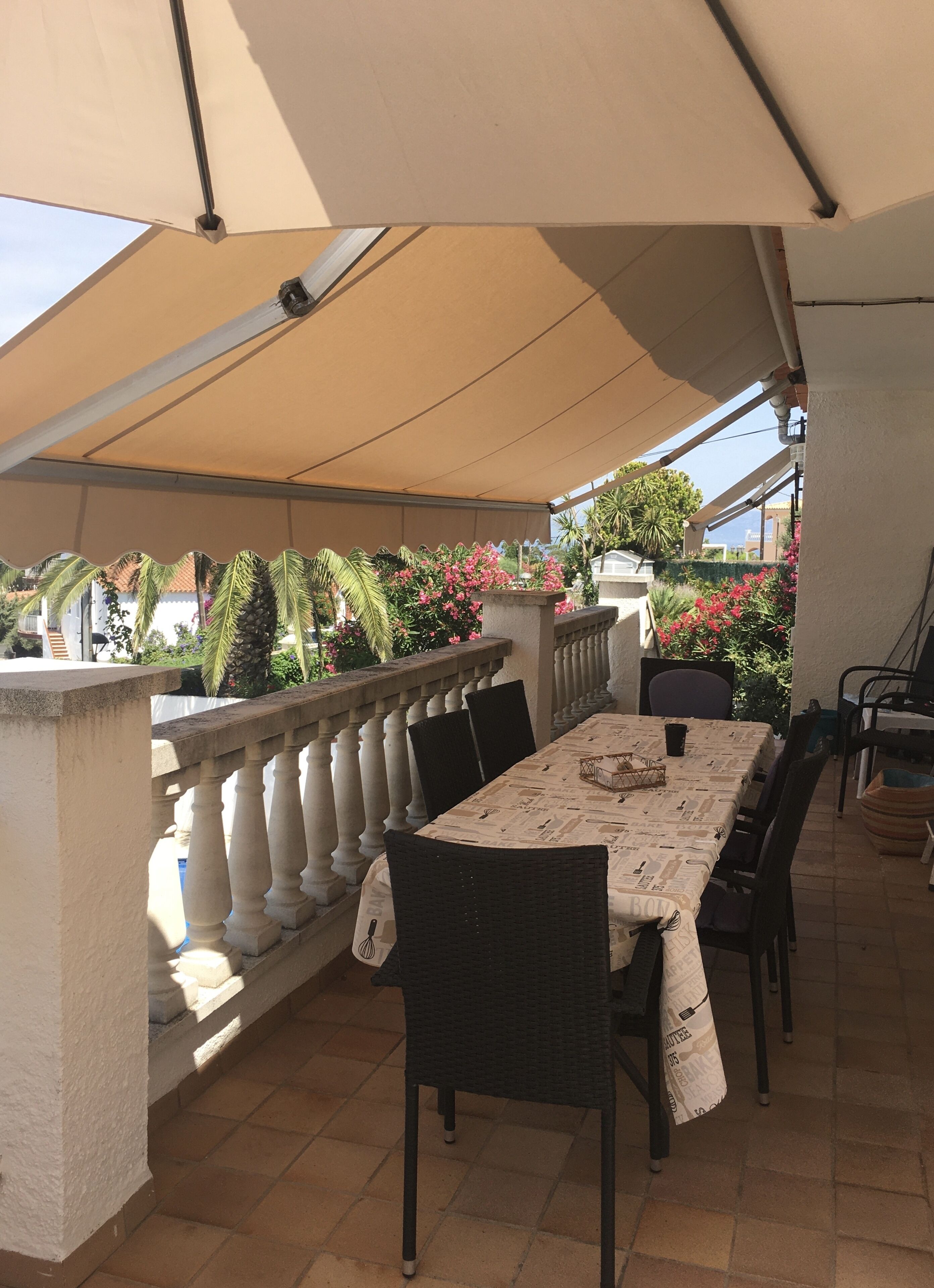 Patio esterno con tavolo e sedie sotto una tettoia, e ringhiera.
