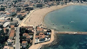 Vista aérea de una ciudad costera con una playa de arena, edificios residenciales y un mar azul cristalino.