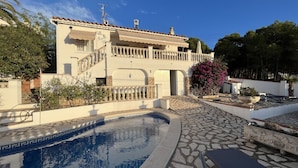 Una casa de dos pisos con piscina, una escalera y un jardín con flores rosas.