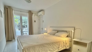 Un dormitorio con cama, mesita de noche, cortinas en la ventana y un equipo de aire acondicionado.