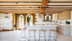 Une cuisine moderne dotée d’un grand îlot central, de poutres en bois et de tabourets de bar.