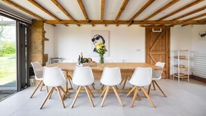 Un coin repas avec une table en bois, des chaises blanches et un vase rempli de fleurs.