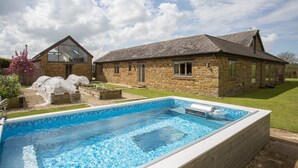 Une maison en pierre avec une piscine, un jardin et un ciel dégagé.