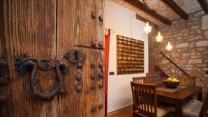 A rustic wooden door with a metal ring handle, a stone wall, and a dining area with wooden chairs and a table. - Casa Anita - Village House With Charming (Ses salines)