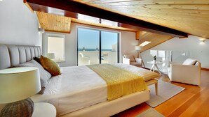 Ein Schlafzimmer mit einem großen Bett, einer Couch, einem kleinen Tisch und Blick ins Freie.