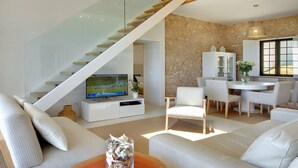 Ein modernes Wohnzimmer mit einer Glaswendeltreppe, weißen Möbeln, einem Essbereich und einer Steinwand.