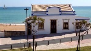 Ein Küstengebäude mit Ziegeldach, einer Tür und Fenstern, nahe einem Strand mit einem Segelboot im Hintergrund.