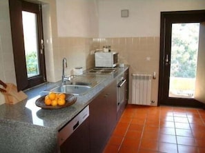 A kitchen with a granite countertop, a sink, a dish rack, and a bowl of oranges.