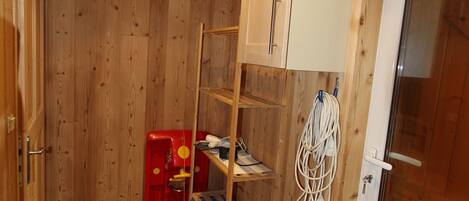 A compact room with wooden walls, a tiled floor, a white door, and a small shelving unit with various items.