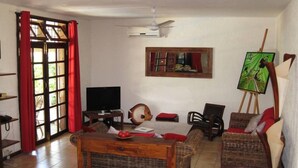 A living room with a television, a painting on a stand, wicker furniture, and a red curtain.