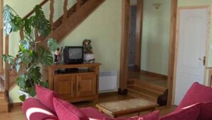 A living room with a wooden staircase, a television on a wooden cabinet, and a red sofa. - country holiday home - 7 rooms - 5/6 persons (Labrousse)