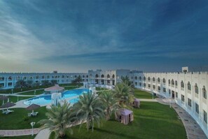 A courtyard with a pool, palm trees, and a building with arched windows.
