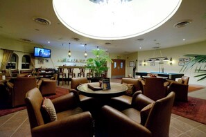 A hotel lobby with leather seating, a pool table, a bar area, and a television.