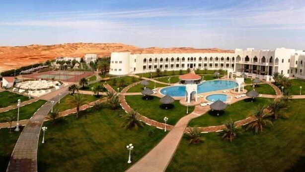 A hotel with a large central pool, multiple guest rooms, and a desert landscape in the background. - HOTEL (Abu Dhabi)
