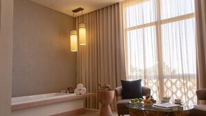 A modern bathroom with a bathtub, a wooden stool, and a glass table with a book and fruit. - HOTEL (Abu Dhabi)