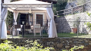 A covered outdoor seating area with a stone wall, metal railing, and a pergola. - Elegant escape sea view private pool & gardens perfect starting point MTB&hiking (Alassio)