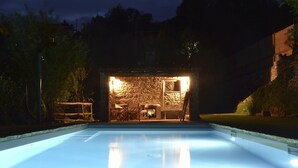 A swimming pool with a stone wall and seating area at night. - Elegant escape sea view private pool & gardens perfect starting point MTB&hiking (Alassio)