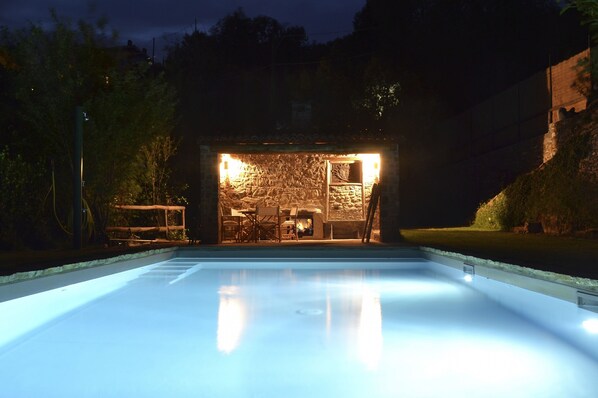 Una piscina con pared de piedra y zona de estar por la noche.