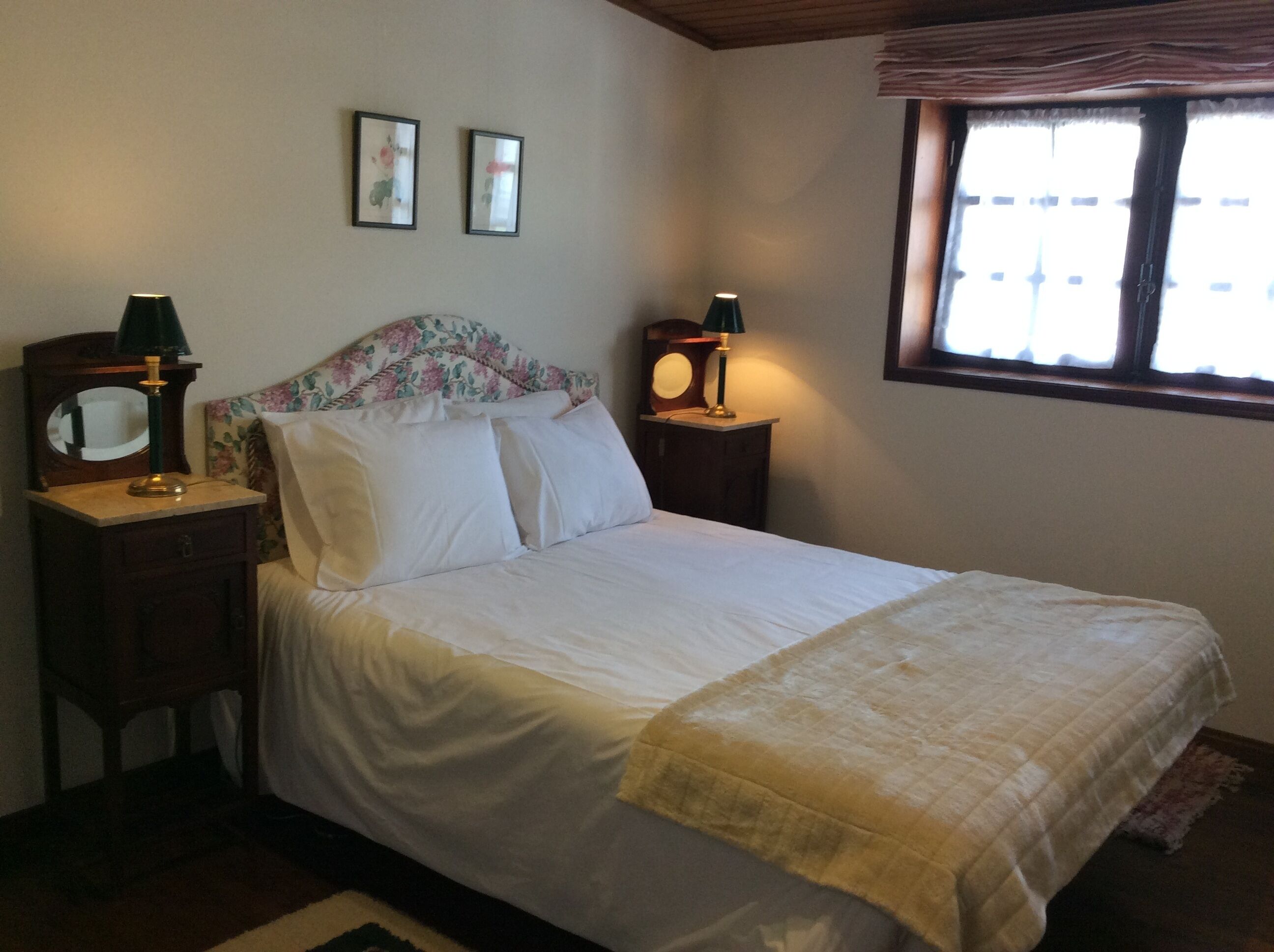Un dormitorio con cama, dos mesitas de noche, un espejo y una ventana con persianas.
