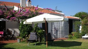 En baghave med en overdækket terrasse, en pool og et hus med tegltag.