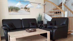 En stue med en sort lædersofa, et træbord og en trappe i baggrunden.