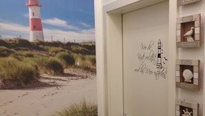 Et værelse med en dør prydet med et marint klistermærke, en plakat med et strandmotiv og en lille potteplante.