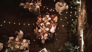 Un espace de restauration en plein air avec plusieurs tables disposées sous des guirlandes lumineuses, le tout entouré de verdure.