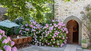 Un bâtiment en pierre doté d’une porte en bois, entouré de buissons d’hortensias aux fleurs d’un rose éclatant.