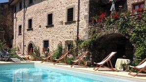 Un bâtiment en pierre doté d’une piscine, de chaises longues et de plantes en pot.