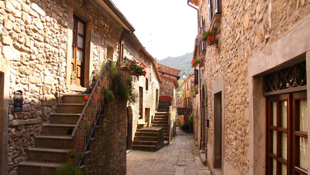 Un étroit sentier de pierre, bordé de bâtiments aux portes et fenêtres en bois, mène à un escalier en pierre.
