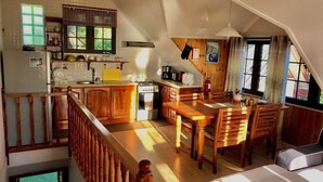 Un'ampia cucina con mobili in legno, una zona pranzo con tavolo e sedie, e un soppalco con zona notte e vista sull'esterno.