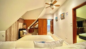 Una camera da letto con soffitto spiovente, un letto, un armadio in legno e una ventola a soffitto.