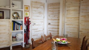 Un comedor con una mesa de madera, sillas, una estantería y un arreglo floral decorativo.