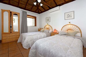 Ein Schlafzimmer mit zwei Betten, einem Holzschrank, einem Fenster mit Vorhängen und einem Deckenventilator.