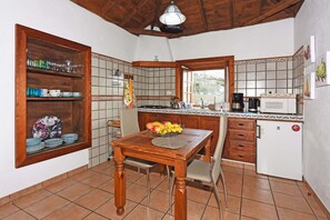 A kitchen with a wooden table, chairs, a fruit bowl, a coffee maker, and a refrigerator.