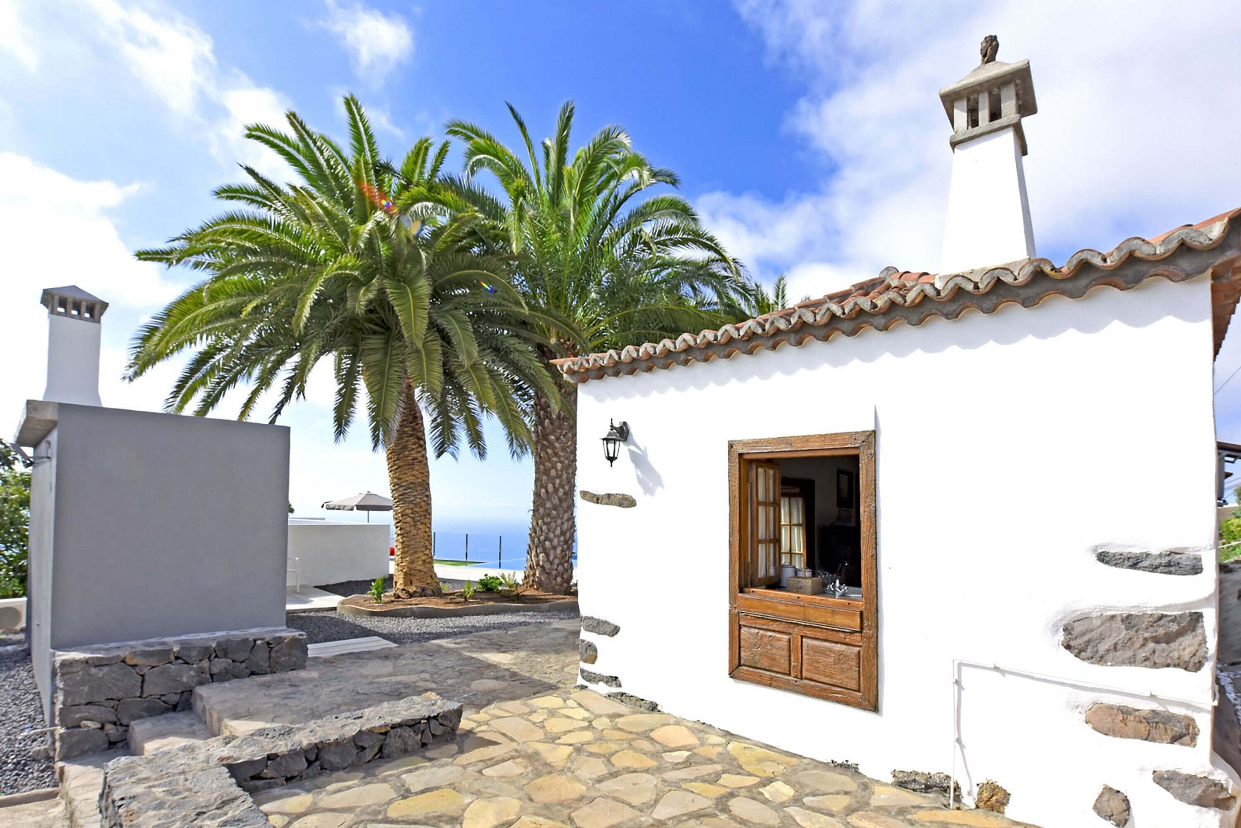 A white building with a tiled roof, a wooden door, and a stone staircase leading to the entrance.