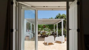 Eine offene Schiebetür führt zu einer Terrasse mit Gartenmöbeln und einer Pergola.