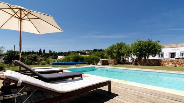Eine Holzterrasse mit Pool, Liegestühlen und Sonnenschirm.