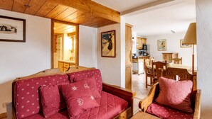 Ein gemütliches Wohnzimmer mit Holzbalkendecke, einem roten Sofa mit herzmusterten Kissen und einem Essbereich mit Holzmöbeln.