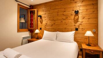 A hotel room with a wooden headboard, a bed with white linens, two bedside lamps, and a window with a curtain.