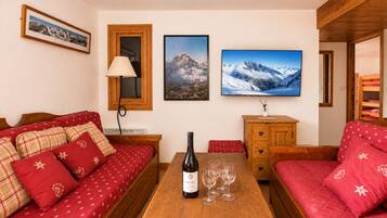 A cozy room with a wooden table, a sofa, a cabinet, and a bed with red bedding.