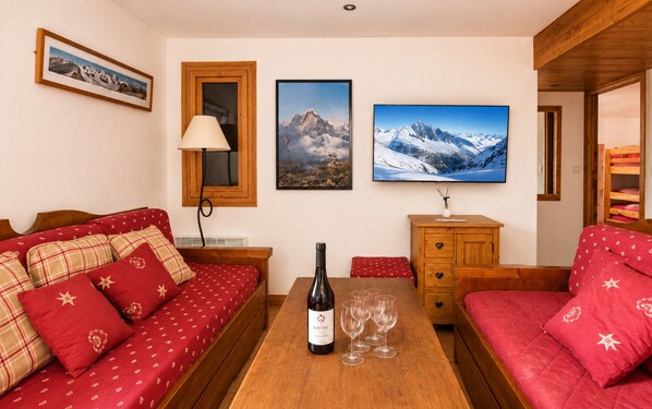 A cozy room with a wooden table, a sofa, a cabinet, and a bed with red bedding.