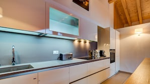 A modern kitchen with a long countertop, built-in oven, and a wooden ceiling.