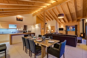 Un amplio salón con techo de madera, un sofá, una mesa de comedor para cuatro comensales y una cocina al fondo.