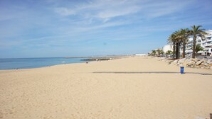 Una amplia playa de arena con cielo despejado, un rompeolas rocoso y palmeras.
