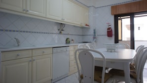 Una cocina con armarios blancos, salpicadero de azulejos y un comedor con mesa y sillas blancas.
