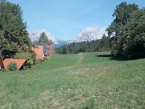 Un campo cubierto de hierba con un edificio a la izquierda y montañas nevadas al fondo.
