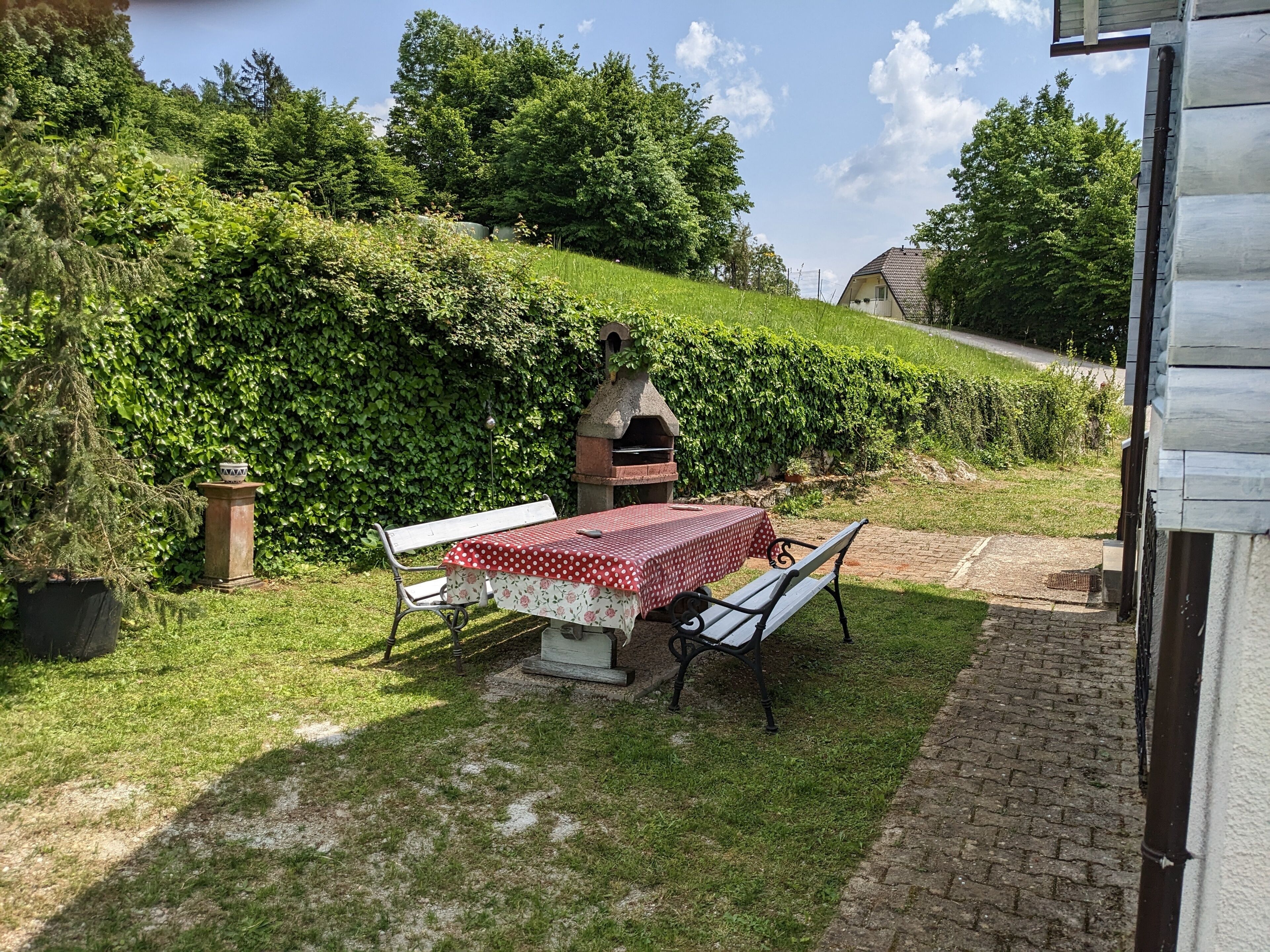 Eine Terrasse mit Tisch und Bänken, umgeben von üppiger Vegetation und einem Ziegelweg.