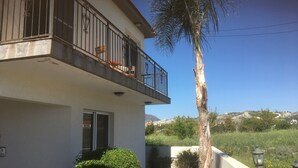 A two-story building with a balcony, a small garden, and a view of hills in the background. - Private Pool, Private Location, Free Wifi, All Day Sunbathing in private garden (Alethriko)