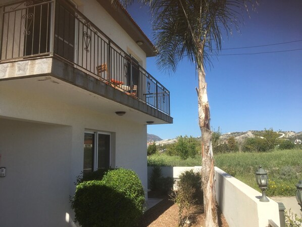 A two-story building with a balcony, a small garden, and a view of hills in the background. - Private Pool, Private Location, Free Wifi, All Day Sunbathing in private garden (Alethriko)
